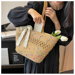 Détail d'un sac cabas en paille tressée avec pompons colorés et nœud en dentelle blanche