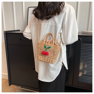 Close-up of handwoven straw crossbody bag with red cherry crochet decor and drawstring liner
