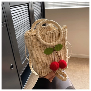Macro shot of hand-woven straw bucket bag featuring 3D red cherry accents and drawstring liner