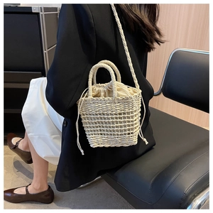 Detail of hand-woven straw bucket bag featuring a drawstring closure and beige woven straps
