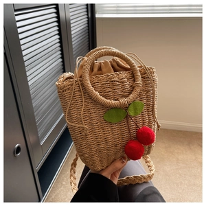 Macro view of woven straw bag featuring red cherry charms and beige drawstring lining