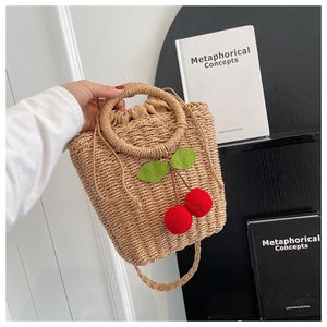 Detail of handmade woven straw bag with decorative red cherry pom-poms and drawstring liner