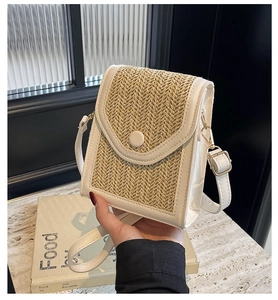 Detail of handwoven straw crossbody bag with white leather trim and gold metal hook