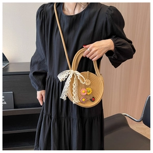 Detailansicht der runden Strohtasche mit Gänseblümchen-Anhängern und weißer Spitzenschleife