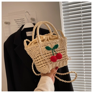 Close-up of hand-woven straw bag featuring red crochet cherry accents and drawstring liner