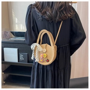 Detailansicht einer runden Strohtasche mit Spitzenschleife und Blumenakzenten
