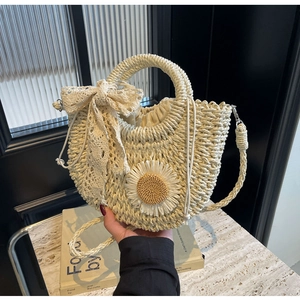 Detail of hand-woven straw bag featuring daisy applique and lace bow on a beige surface