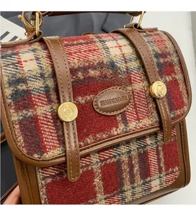 Nahaufnahme von rot-braunem Karostoff und Ledergriff mit Metallschnallen an Handtasche