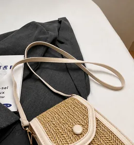 Detail of handwoven beige straw crossbody bag with leather strap and snap closure
