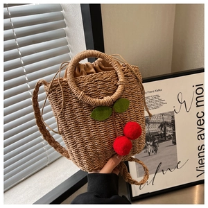 Detail of woven straw handbag with red cherry accents and drawstring closure under soft light