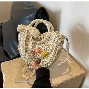 Detail of hand-woven straw bag featuring 3D floral accents and a delicate lace bow
