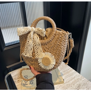 Close-up of semi-circular straw woven bag with lace bow and daisy pendant detail