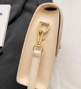 Close-up of golden hardware swivel hook and beige leather side seam on a shoulder bag