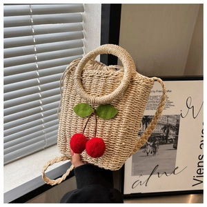 Detail of woven straw bag with cherry pompoms and drawstring lining on a neutral background