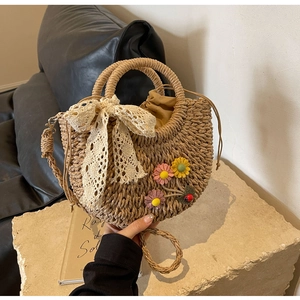 Detail of hand-woven straw bag featuring decorative flowers and cream lace bow
