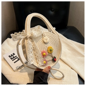 Detail der runden beige geflochtenen Tasche mit Spitzenschleife und Stoffblumen-Deko