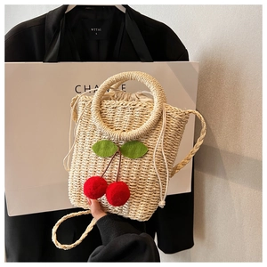 Detail of hand-woven straw crossbody bag with red cherry accents and drawstring closure