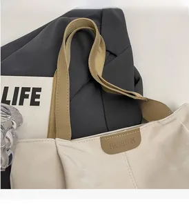 Detail of light beige tote bag featuring reinforced handles and embossed fashion label