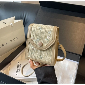 Détail d'un sac bandoulière en paille beige avec broderie florale et finitions en cuir kaki
