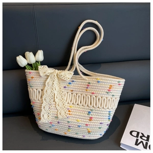 Détail d'un sac de plage tressé avec pompons colorés et nœud en dentelle décoratif
