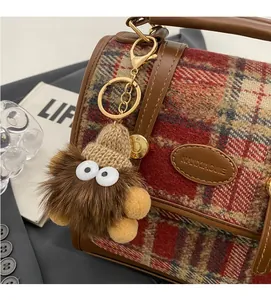 Detailansicht eines braunen Plüschmonsters mit Strickmütze an einer braunen Ledertasche