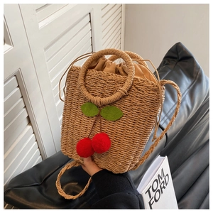 Detail of straw woven handbag with cherry charms on black leather sofa with book