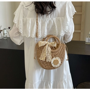 Detail of straw woven crossbody bag with lace bow and daisy decor on a model in white dress