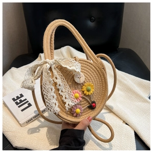 Detail der runden Strohtasche mit weißer Spitzenschleife und Stickblumen auf schwarzem Stuhl