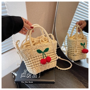 Detail of straw bucket bag with crochet cherries, drawstring lining, and long strap