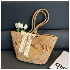 Détail du sac cabas beige tissé à la main avec pompons colorés et nœud en dentelle blanche