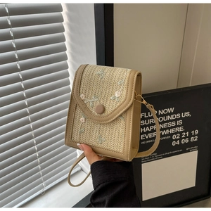Détail d'un sac à bandoulière carré brodé de fleurs avec rabat tissé tenu à la main