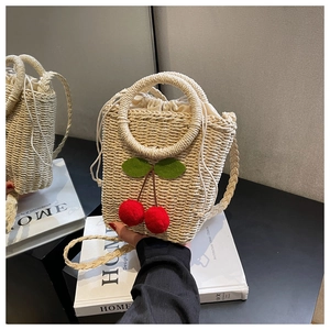 Detail of beige straw bucket bag featuring red cherry charms and drawstring lining