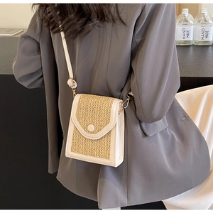Detail of hand-woven straw crossbody bag with white leather trim and round buckle