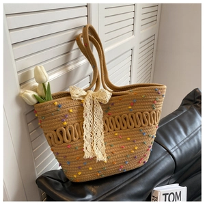 Détail d'un sac cabas en paille tissée avec pompons colorés et un gros nœud en dentelle