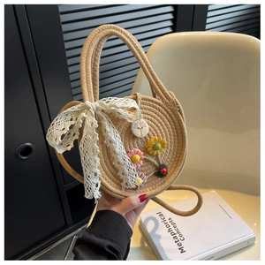 Detail einer runden Strohhandtasche mit Spitzenschleife und floralen Akzenten