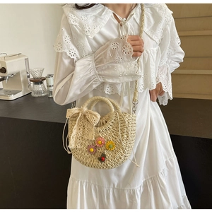 Detail of hand-woven straw crossbody bag with floral accents and a lace bow detail