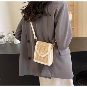 Detail view of a woven straw crossbody bag with white leather trim worn by a model