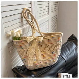 Détail du sac de plage tissé beige avec pompons colorés et un nœud en dentelle