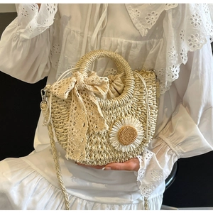 Detail of handmade woven straw crossbody bag with white daisy flowers and lace bow