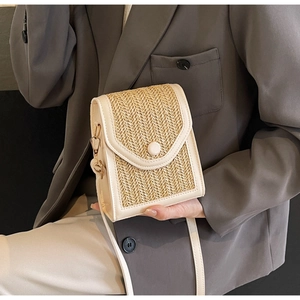 Detail view of woven straw shoulder bag with beige leather trim and round buckle decoration
