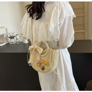 Detail of hand-woven straw bag with colorful floral decor and lace ribbon bow