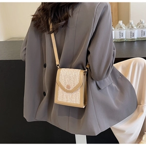 Detail of hand-woven beige straw crossbody bag with leather trim on model outfit