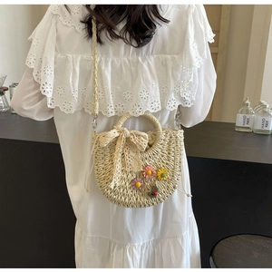 Detail of handmade straw crossbody bag with floral lace accents shown on a model