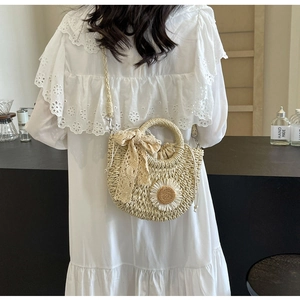 Detail of hand-woven straw crossbody bag with white daisy decor and lace bow on model