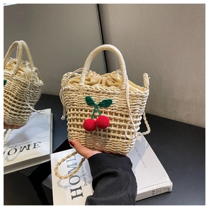 Detail of handmade woven straw bag featuring red crochet cherry accents and drawstring liner