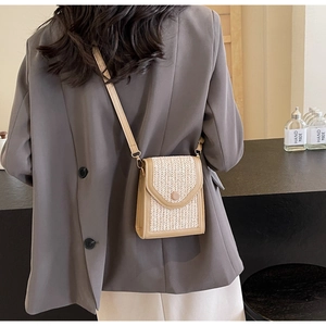 Close-up of handmade woven straw crossbody bag with brown leather trim and slim strap