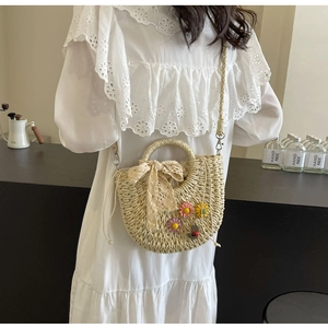 Detail of woven straw handbag with lace bow and floral accents on a crossbody strap