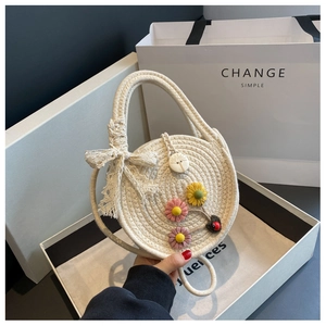Detailansicht einer cremefarbenen runden Handtasche mit 3D-Blumenakzenten und Marienkäfer-Anhänger