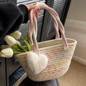 Handgewebte Stroh-Eimertasche mit bunten Akzenten und Plüschherz-Anhänger auf weißem Grund
