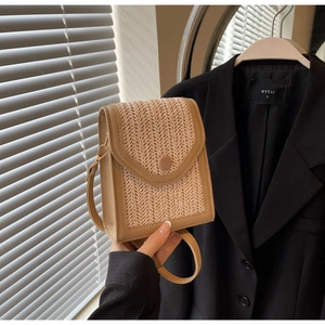 Close-up of hand-woven straw crossbody bag with khaki leather trim and round buckle